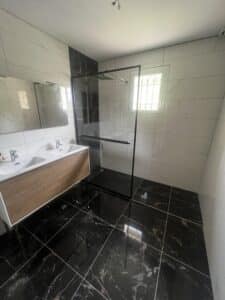 Salle de bain contemporaine avec carrelage marbré blanc et noir, meuble double vasque en bois, douche à l'italienne et fenêtre.